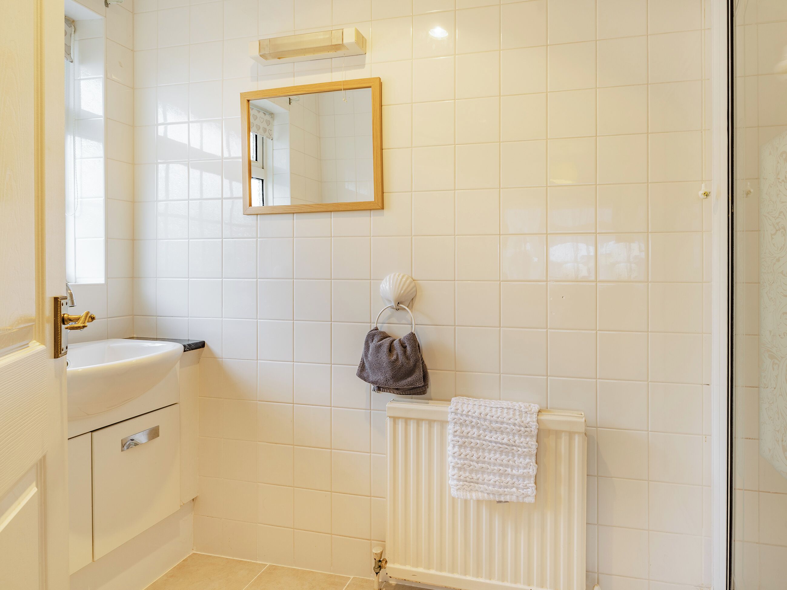 A bathroom with white tiles, a sink, a mirror, and a towel rack.