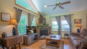 A cozy living room with a fireplace, wooden furniture, and large windows with curtains.
