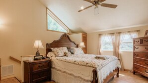 A bedroom with a wooden bed, two bedside tables, a dresser, and a ceiling fan.