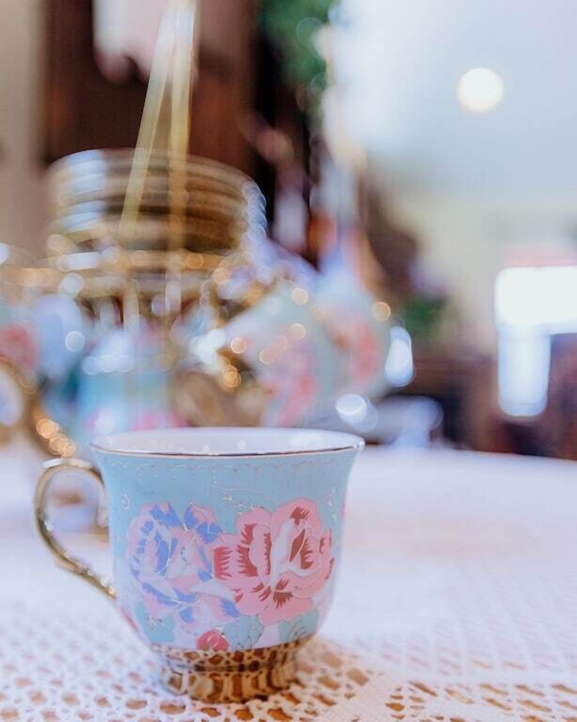 A close-up of a floral-patterned cup on a lace tablecloth.