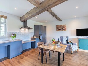 Una cocina moderna con una isla central, un comedor con una mesa para dos, y una sala de estar con televisor y sofá.