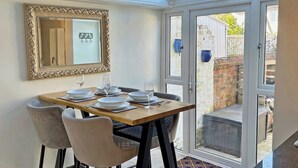 Un comedor con una mesa dispuesta para cuatro, un espejo grande y decorativo, y un portón de cristal que da a un espacio exterior.