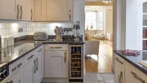 Una cocina moderna con alacenas blancas, un refrigerador para vinos empotrado y una cafetera.