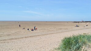 Una extensa playa de arena abierta con algunas personas dispersas, algunas sentadas y otras caminando.