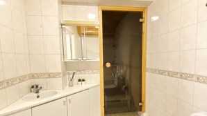 Ein Badezimmer mit weißen Fliesen, einer Holzbalkendecke, einem Waschbecken mit Spiegel und einer Toilette.