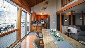 A spacious living area with a wooden ceiling, a dining table with candles, and a view of the kitchen and outdoor seating. - Cozy Cottage with beautiful Mountain View’s - close to wineries (Wintergreen Resort)