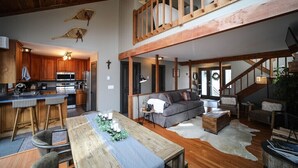 A spacious living area with a high ceiling, wooden beams, a dining table with candles, a sofa, and a staircase leading to an upper level. - Cozy Cottage with beautiful Mountain View’s - close to wineries (Wintergreen Resort)