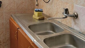 Una cucina con due lavelli in acciaio inossidabile, un armadietto in legno con maniglie dorate e uno scaldacqua bianco montato a parete.