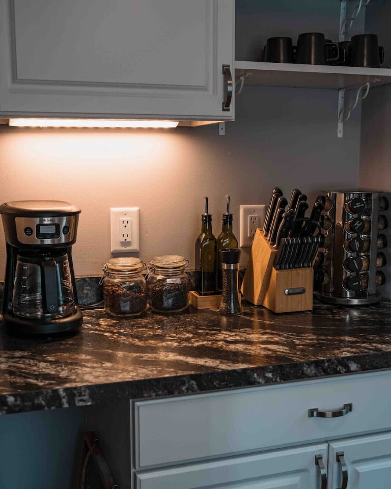 A kitchen with a coffee maker, jars, a knife block, and a countertop.