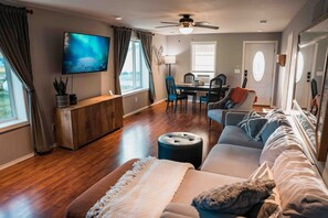 A living room with a sofa, ottoman, and a TV mounted on the wall.
