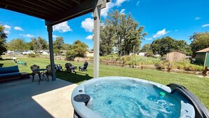A hot tub under a covered patio with a grassy area and outdoor furniture.