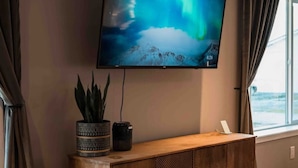 A room with a TV mounted on the wall, a wooden cabinet below, and a window with curtains.