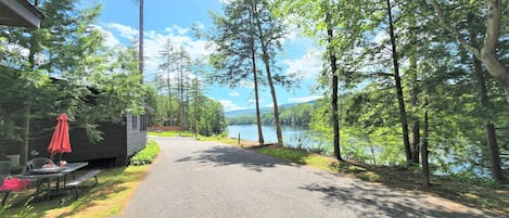 A cabin with a picnic table and red umbrella, surrounded by trees and a lake.