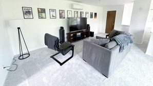 A living room with a grey sofa, a black chair, a TV, and framed pictures on the wall. - Beautiful Mountain Getaway with amazing views (Loch Lomond)