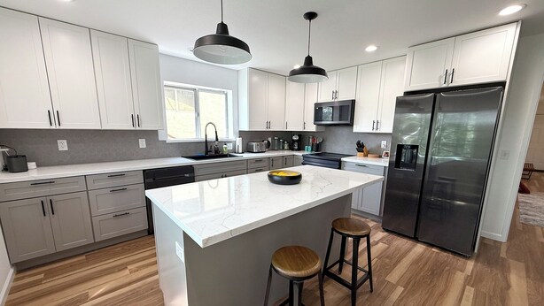 A modern kitchen with white cabinets, a central island, two bar stools, a stainless steel refrigerator, and pendant lighting. - Beautiful Mountain Getaway with amazing views (Loch Lomond)