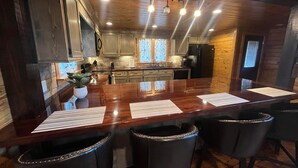A modern kitchen with a central island, bar stools, and a dining area.