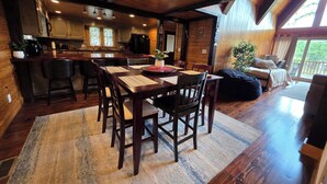 A cozy cabin interior with a dining area, kitchen, and a large window offering a view of the outdoors.