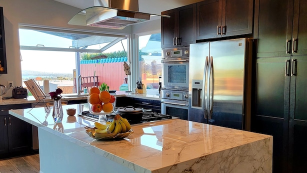A modern kitchen with a large island, stainless steel appliances, and a view of the outdoors.