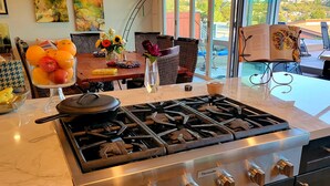 A modern kitchen with a stainless steel stove, a dining area with a table set for two, and a large window offering a view of the outdoors.