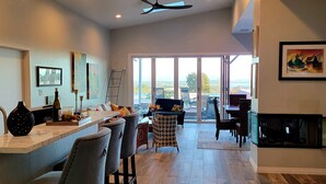 A modern kitchen with a bar area, a dining space, and a view through large sliding glass doors.