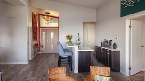 A modern kitchen with dark cabinets, a white countertop, and a bar area. There is a dining area with wicker chairs and a small table.