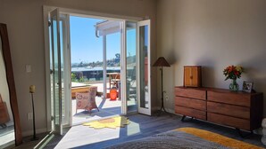A spacious room with a sliding glass door leading to a balcony, a wooden dresser, a floor lamp, and a vase with flowers.