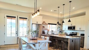 A modern kitchen with white cabinets, a central island with bar stools, and pendant lighting. - Kanab Getaway Red Mesa Ranch, Near Zion, Amazing Red Rock & Starry Night Views! (Kanab ( Will Show as Canyon City on Some Apps))