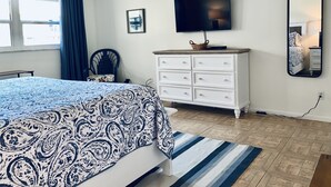 Une chambre à coucher avec un lit, une commode, un téléviseur, une chaise et une fenêtre avec des rideaux.