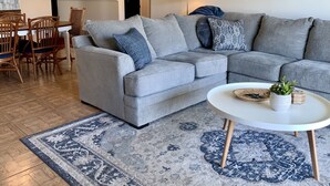 Un salon avec un canapé d’angle gris, une table basse ronde et un tapis bleu à motifs.