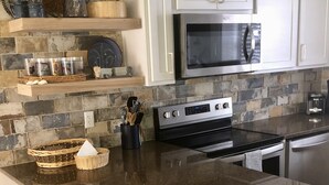Une cuisine dotée d’un plan de travail en granit, d’appareils électroménagers en acier inoxydable et de tabourets de bar en osier.