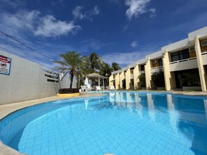 Piscina com bordas azulejadas, área de estar coberta e um edifício com varandas múltiplas.
