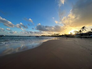 Uma praia com céu claro, mar calmo e alguns barcos.