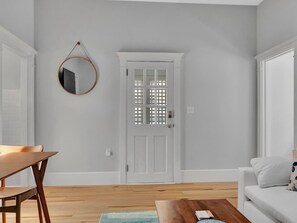 A room with a white door, a round mirror on the wall, a wooden dining table, and a white sofa.
