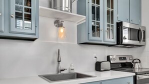 Eine moderne Küche mit hellblauen Schränken, einer Edelstahlspüle, einer eingebauten Mikrowelle und einem Wasserkocher auf dem Herd.