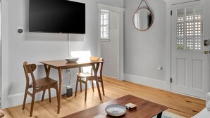 Ein Essbereich mit Holztisch und -stühlen, einem an der Wand montierten Flachbildfernseher und einer Tür mit Gitterverzierungen.