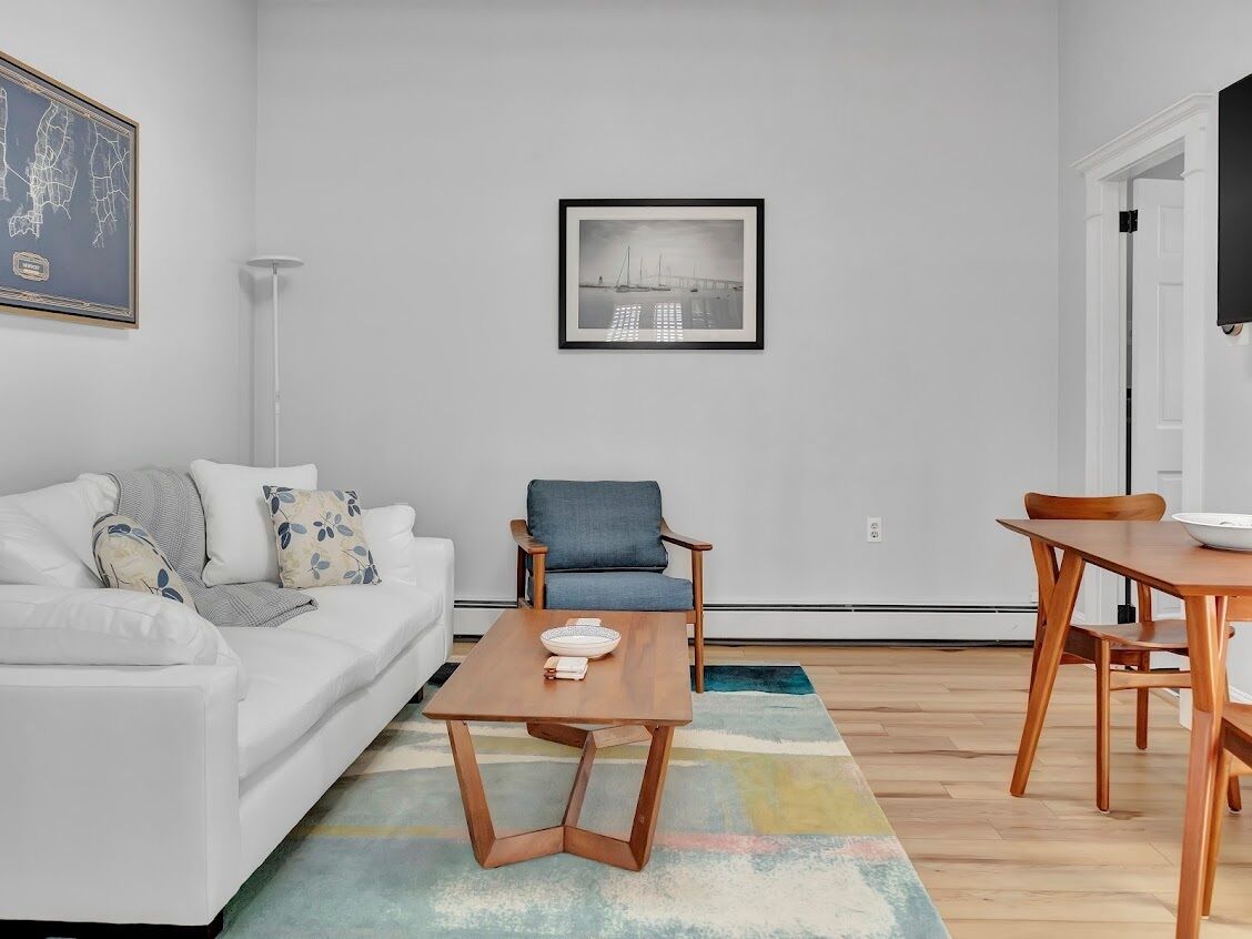 A modern living room with a white sofa, a blue armchair, a wooden coffee table, and a framed black and white photograph on the wall.