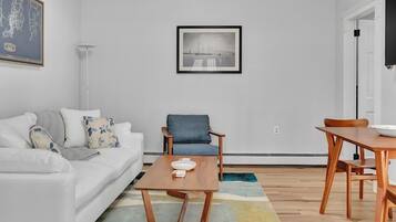 A modern living room with a white sofa, a blue armchair, a wooden coffee table, and a framed black and white photograph on the wall.