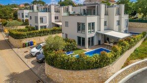 A modern multi-story residential building with a swimming pool, stone retaining walls, and a paved driveway. - Modern villa MODERNA with heated pool, hot tub and sauna (Malinska)