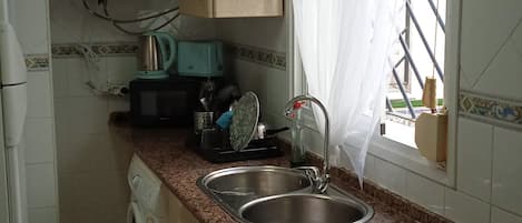 A compact kitchen with a washing machine, microwave, sink, and stove.