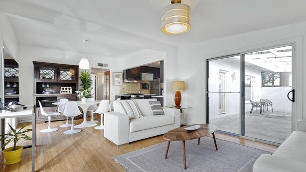 A modern living room with a white sofa, a coffee table, and a dining area with white chairs. There is a kitchen in the background with a microwave and cabinets. - ICONIC MID-CENTURY MODERN  “HAVER HOME” (Scottsdale)