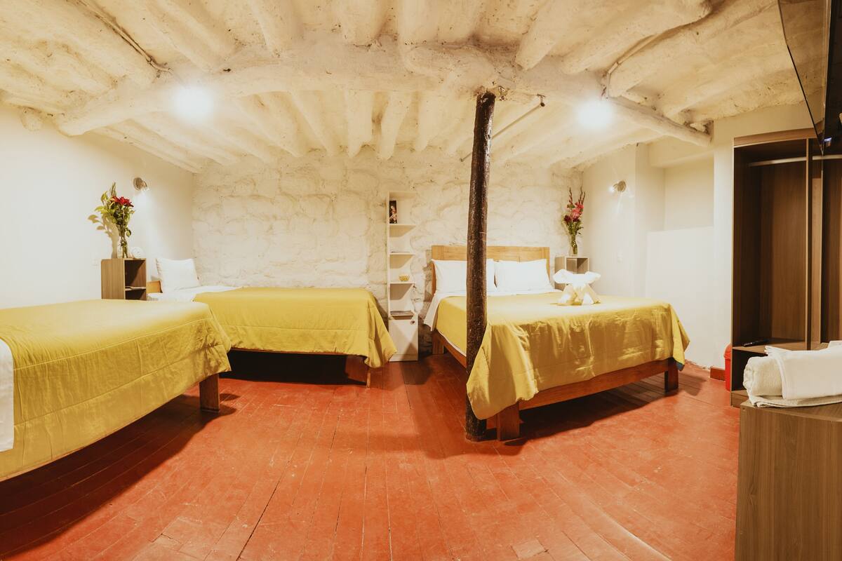 Una habitación con dos camas, un armario de madera, una estantería con libros y suelo de ladrillo.