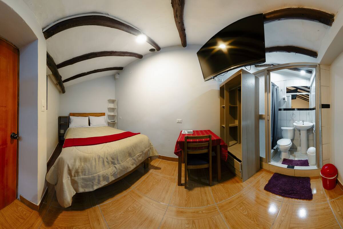 Una habitación con cama, una mesa y un baño visible a través de una puerta abierta.