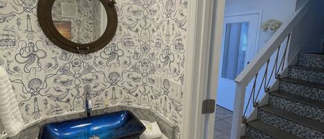 A bathroom with a blue sink, a round mirror, and nautical-themed wallpaper.