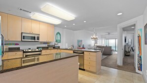 A modern kitchen with a large island, built-in appliances, and a dining area with a view to the living room. - Coveted Gulf-front condo on pool deck, directly on beach, no highway to cross! (Biloxi)