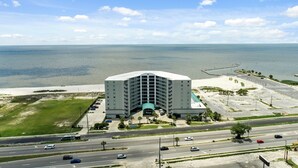 A high-rise hotel with a curved facade, a parking lot, and a view of the ocean. - Coveted Gulf-front condo on pool deck, directly on beach, no highway to cross! (Biloxi)