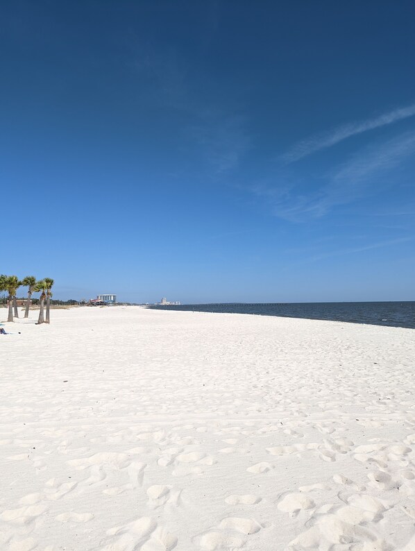 A beach with white sand, palm trees, and a clear blue sky.