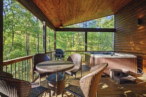 Eine Holzterrasse mit Korbmöbeln, einem Whirlpool und Blick auf einen Wald.