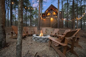 Eine Holzhütte mit einem Steinkamin inmitten eines Waldes, umgeben von Holzstühlen und Lichterketten.