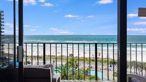 Un balcón con vista al océano y la playa, que cuenta con una piscina y sillones de descanso.