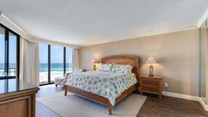 Un dormitorio con una cama grande, lámparas de noche, una mesita de noche, vista al océano y piso de madera.